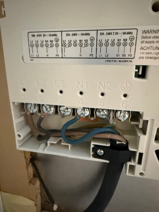 Elektrisk inkopplingsplint med flera ledningar i olika färger anslutna, etikett ovan visar spänningsspecifikationer för 380-415V och 220-240V.