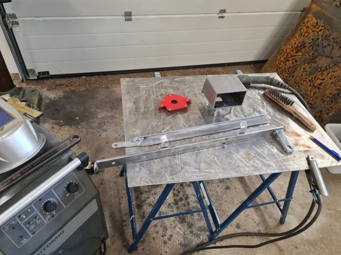 Kapade och svetsade metalldelar placerade på ett bord i ett garage, redo för varmgalvanisering och montering.