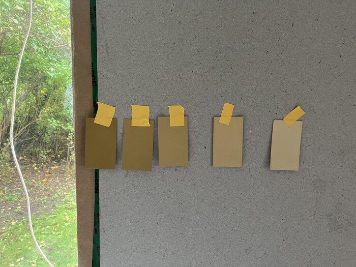Färgprover i olika nyanser av brunt tejpade på en vägg för att testa färger inför ett projekt.