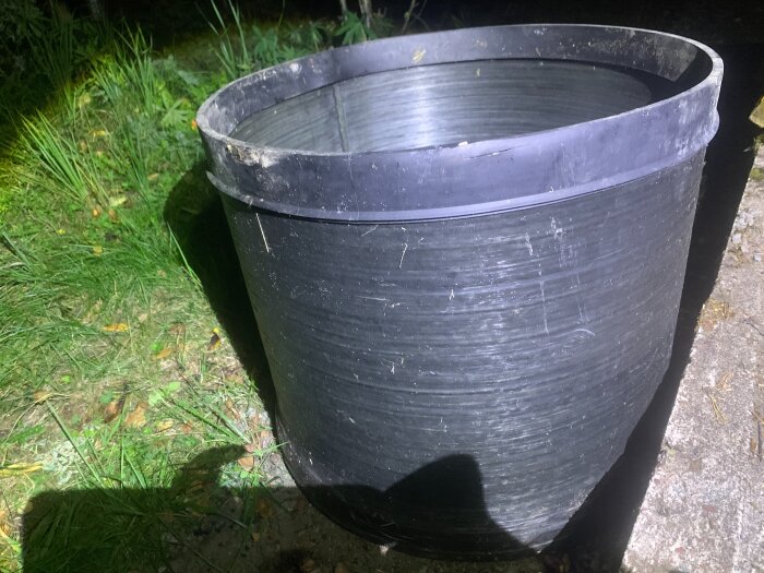 Svart plastförhöjningsring för fördelningsbrunn står på en gräsmatta, fotograferad i mörker med ficklampa.