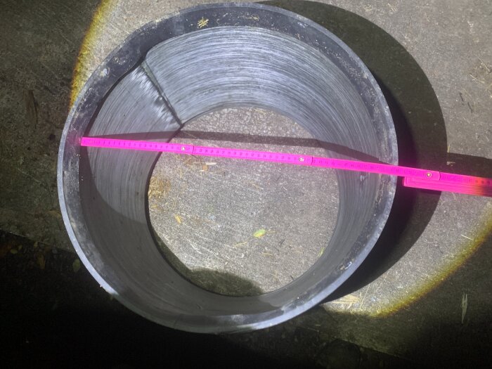 Förhöjningsring av plast på mark med rosa mätsticka tvärs över, används för att höja marknivån kring fördelningsbrunn.