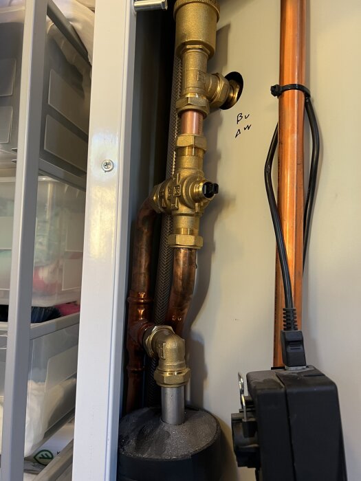 Vattenrör med kopparledningar och en ventilanordning, märkt med "B" och "A" på en vägg i ett teknikskåp, kablar vid sidan.