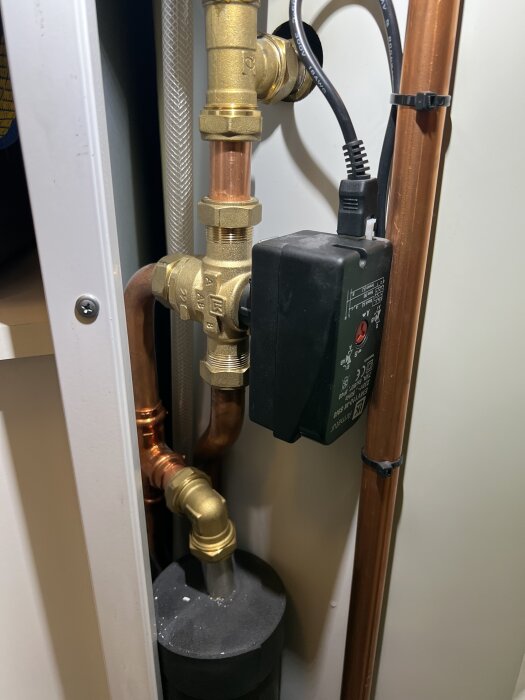 VVS-installation med kopparrör, mässingsbeslag och elektronisk komponent ansluten med sladd.