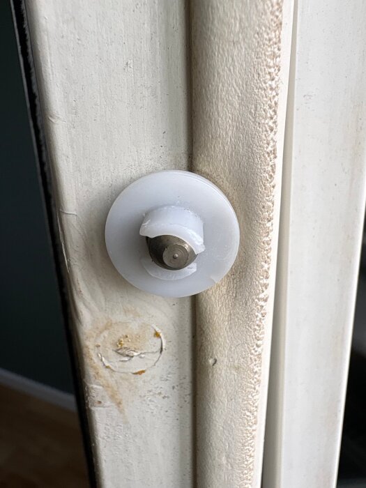Plastdel på fönsterkarm med en synlig skruv, potentiellt trasig, bredvid en skadad del av träramen.