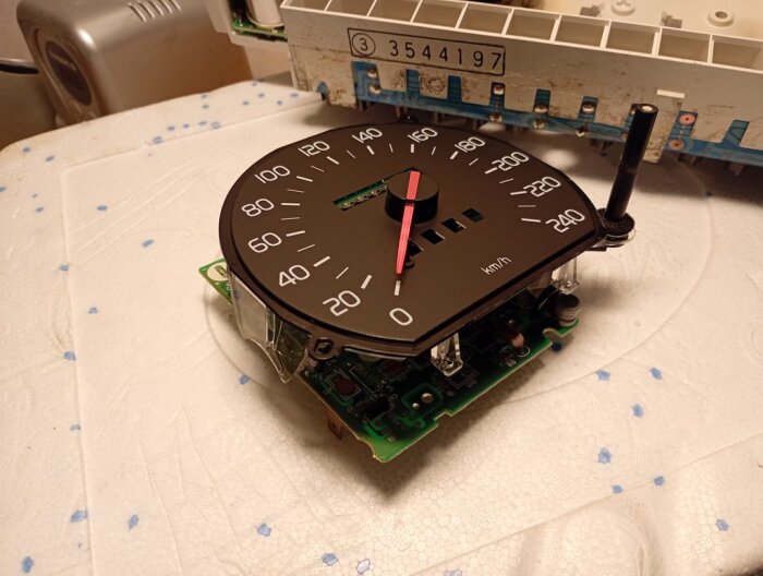 Närbild på en urtagen hastighetsmätare med synliga kretsar och monteringskomponenter på ett elektroniskt kort.