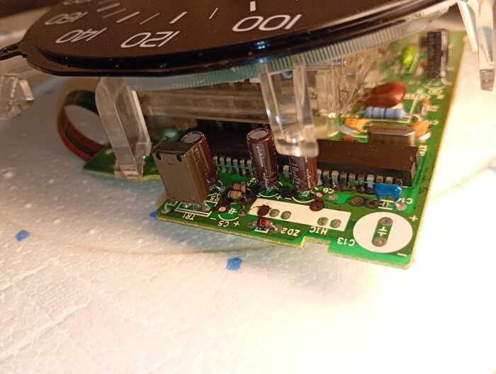 Kretskort med hastighetsmätare, synliga elektrolytkondensatorer och andra elektroniska komponenter, ligger på en vit yta.