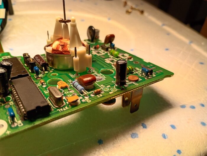 Elektroniskt kretskort med flera komponenter, inklusive kondensatorer och motstånd, placerat på ett underlag med vita och blå prickar.