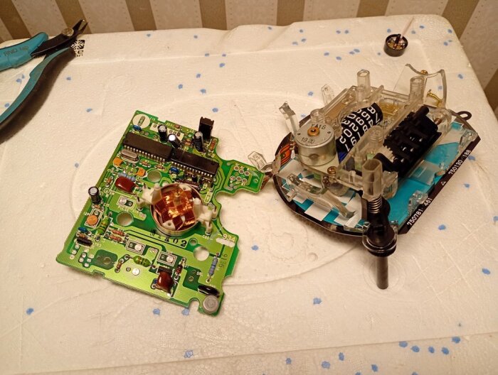 Elektronikkretskort och urtavla från en hastighetsmätare placerade på ett bord, med tång och komponenter i bakgrunden.