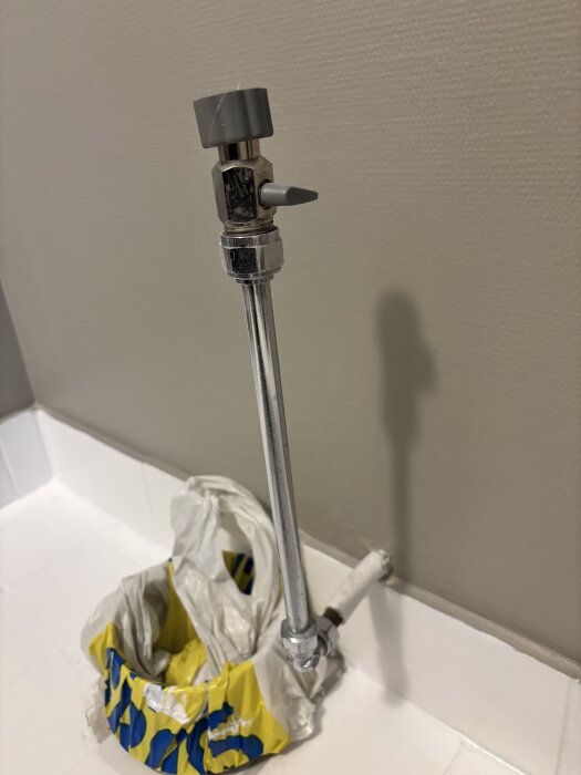 Metallrör med ventil på badrumsgolv, omgivet av en plastpåse som håller det på plats.