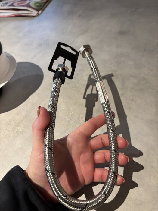 Flexibel metallslang för vattenanslutning hållen i en hand, med kopplingsfäste i ena änden.