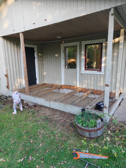 Renovering av tidigare altan till blivande sovrum, synliga bjälkar och plintar, verktyg liggande på marken, barn i pyjamas närvarande.