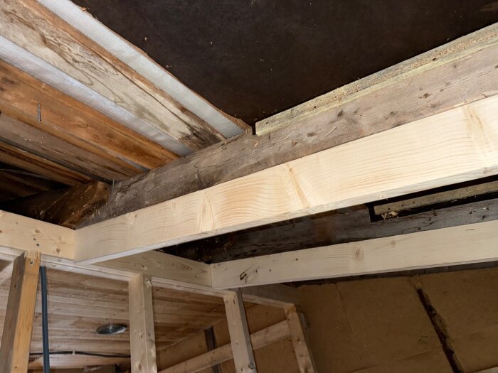 Bild av träkonstruktion i ett tak med synliga bjälkar och isolering; del av en utbyggnad under renovering med frågeställning om isoleringsmetoder.