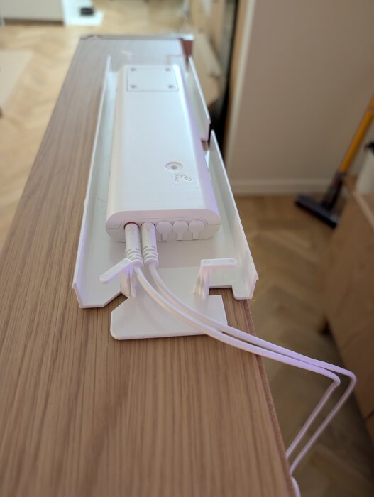 Vit enhet med inkopplade kablar på ett träbord, del av IKEA-spegelskåpets belysningssystem.