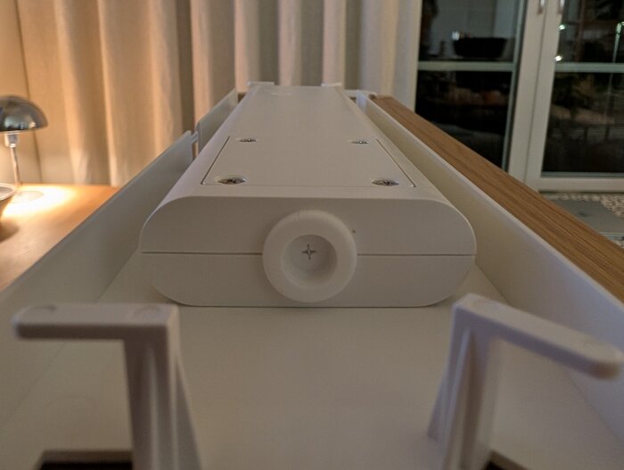 Närbild på baksidan av ett IKEA spegelskåp med infälld belysning, visande anslutningsuttag för kablar, mot en bakgrund av ett rum med gardiner.