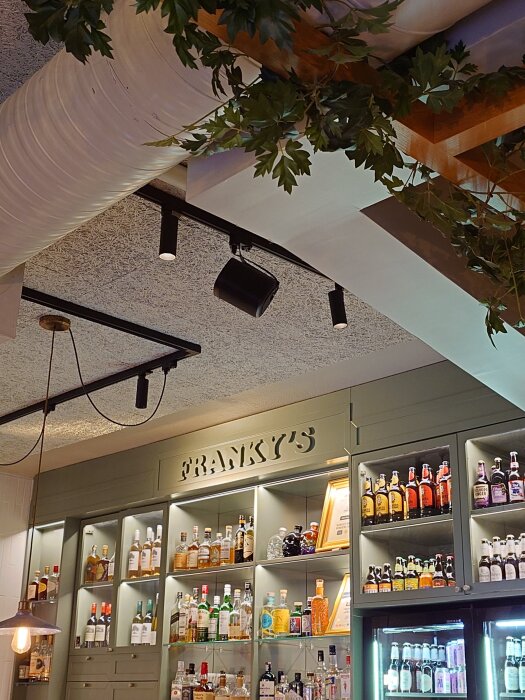 Alkoholdisplay på en bar med texten "FRANKY'S" ovanför. Flaskor är snyggt uppställda på hyllor med flaskor av olika sorter.