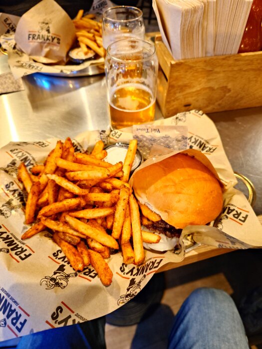 Dubbelburgare med ost och cajunfries serveras på en bricka med öl och servetter vid sidan.