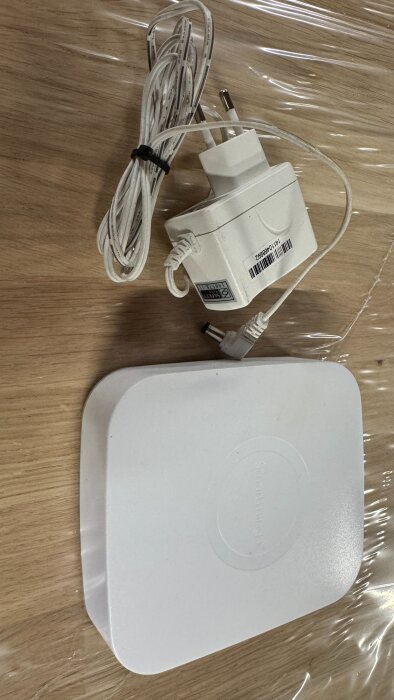 Samsung Smartthings Hub STH-ETH-200 med en D-Link 5V strömadapter visas på ett träbord.