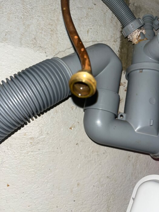 Kopparrör med gängor monterat på en grå plastledning under en diskbänk. Röret ser ut att vara anslutet till en avloppsslang.