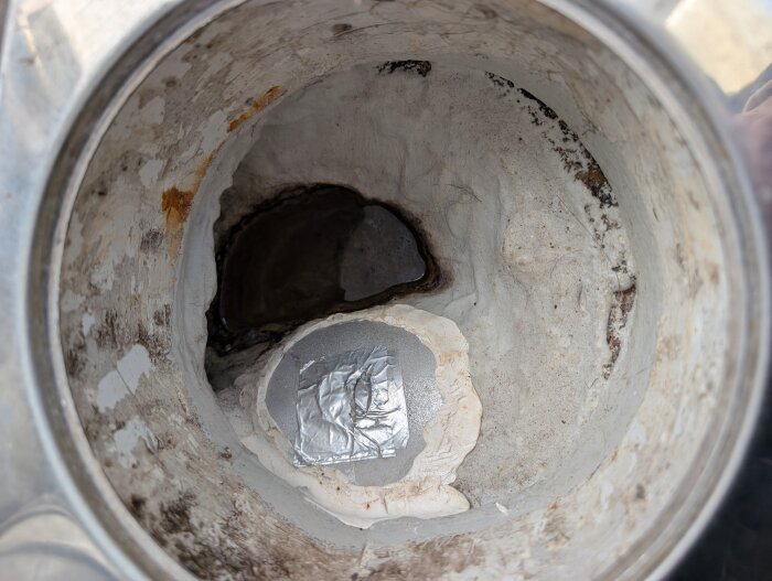 Golvbrunn i ett badrum med slitet ytskikt och tecken på mögel. Silvertejp syns i botten. Diskuteras i samband med eventuell relining av rörsystemet.