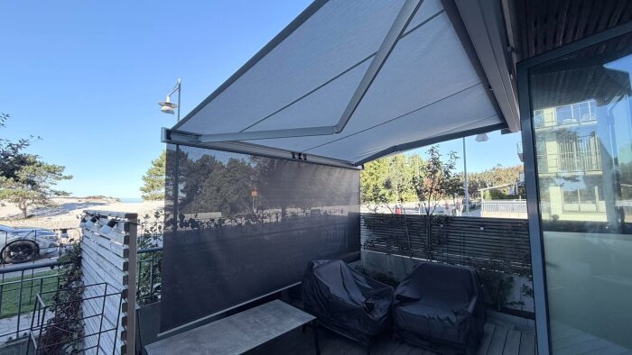 Markis med vertikal zip screen som fungerar som sol- och insynsskydd på uteplats, bredvid fönster och trädgårdsmöbler med skydd.