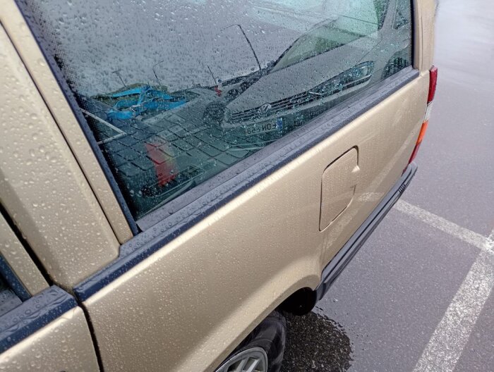 Baksidan av en beige bil på en parkeringsplats med regndroppar på fönstren.