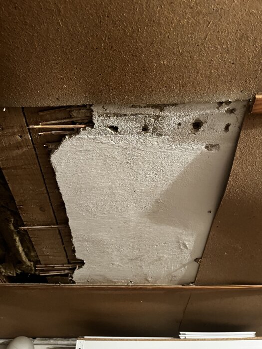 Äldre källartak i ett hus från 20-talet med borttagen panel, vitmålad yta och synliga rör, oro för möjlig asbest i materialet.