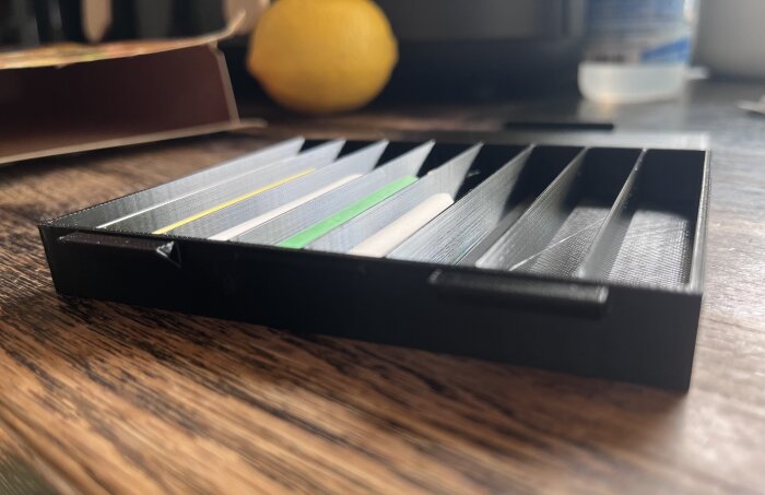3D-printad kritask med olika kritor inuti, placerad på ett bord.