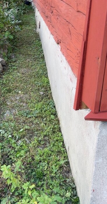 Röd träfasad med lecablockgrund och grönska vid husväggen.