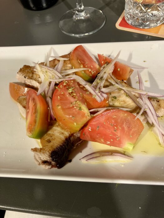 Grillad tonfisk serverad med tomatskivor och lök på en vit tallrik.
