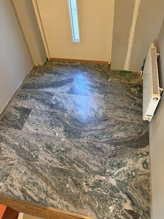 Nytt stengolv installerat i hallen, med ljusgrå och grönbruna nyanser, bredvid en vit vägg och radiator.