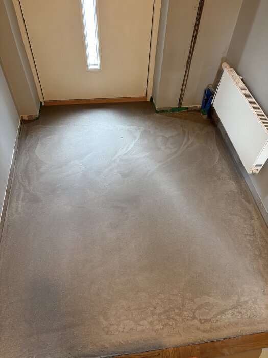 Nyflytspacklat golv i hall med radiatorsystem synligt till höger, redo för vidare behandling med stentvål, med dörr och radiator i bild.