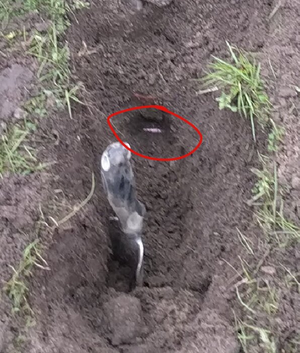 En grävd fårra med en 7mm plastslang markerad i rött, omgiven av jord och gräs, med en spade synlig i förgrunden.