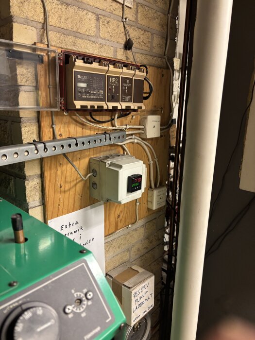 Bilden visar en shuntautomatik installation med en regulator modell TA-230U monterad på en träpanel i en verkstadsmiljö.
