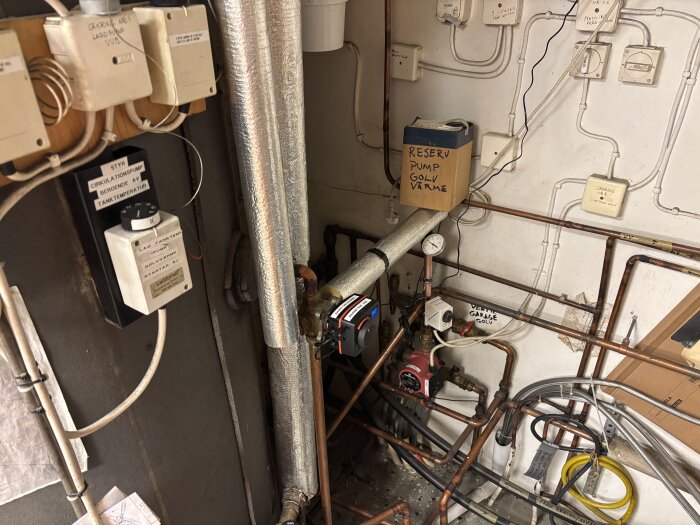 Rörsystem i ett pannrum med installerad ESBE CRA211 regulator och cirkulationspump, omgiven av isolerade rör och olika elektriska komponenter.