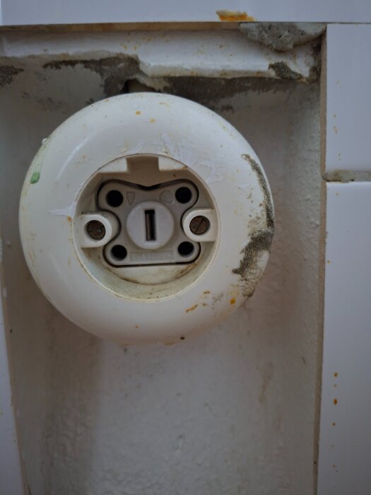 Äldre runt eluttag för 25A, delvis nedsmutsat, monterat i en vit vägg med sprickor och slitage.
