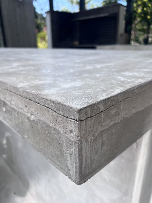 Betongskiva med en tunn spricka nära kanten av en uteköksbänk. Sprickan sträcker sig ca 5 cm in.
