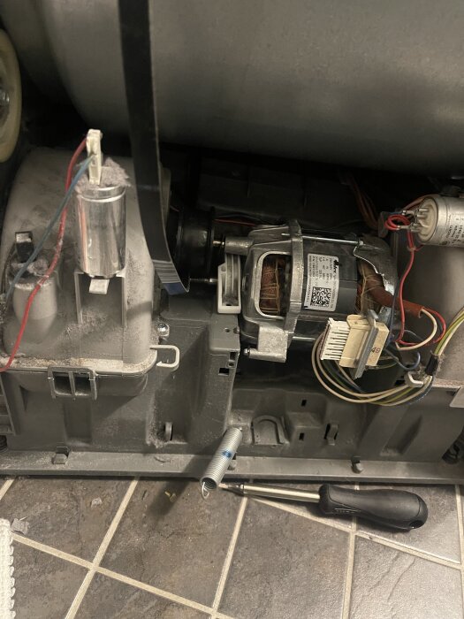 Elektrisk motor och kablar inuti en maskin, med en järnstång och en skruvmejsel på golvet framför.
