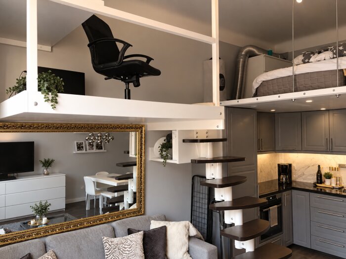 Modern lägenhet med smart loftdesign; spiraltrappa leder till arbetsplats och sovloft ovanför kök med grå skåp, spegel över soffa.