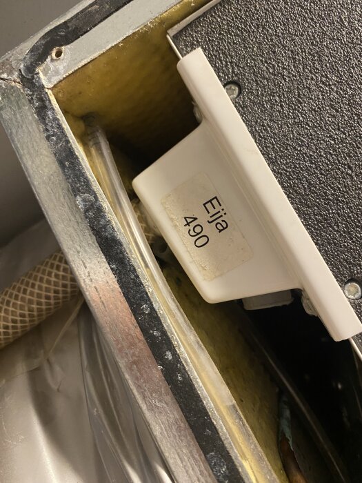 Tryckvakt med etikett "Eija 490" och oanslutna transparenta slangar i botten, installerad i ett skåp med gula väggar och tejp.