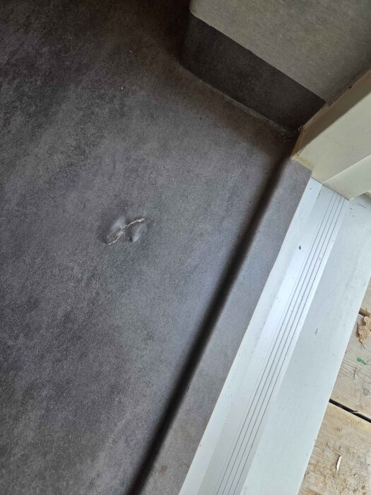 Reva i våtrumsmatta nära dörr, synlig skada på golvets yta, buckla framför värmepump, som nyligen installerats.