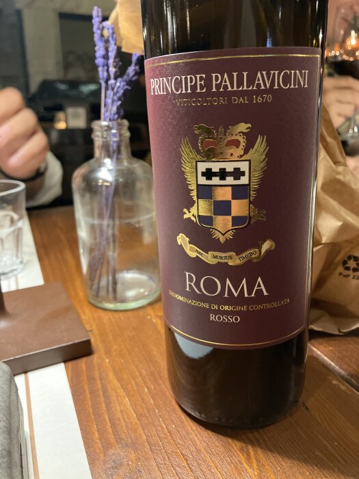 En flaska rött vin, Principe Pallavicini Roma Rosso, står på ett träbord bredvid en glasvas med lavendel.