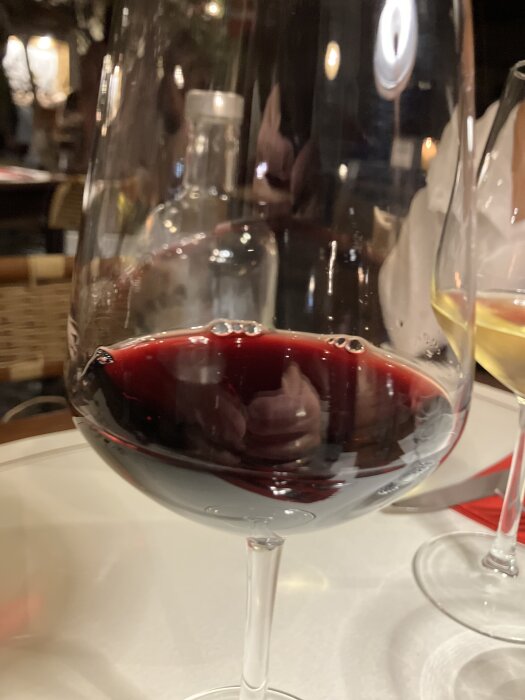 Ett glas rött vin på ett bord, med en flaska i bakgrunden.