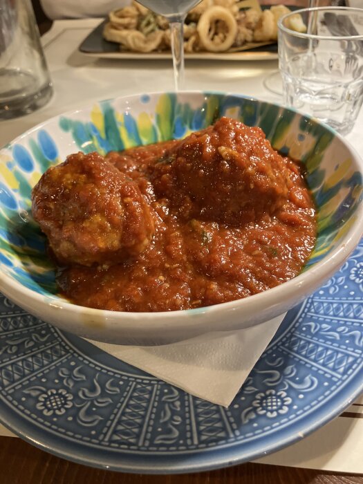 Köttbullar på kalv i tomatsås serverade i en färgglad skål på ett mönstrat fat.