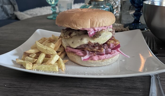 Hemgjord Piteburgare med smält ost, rödlök och rosa sås serverad med pommes frites på en vit tallrik.