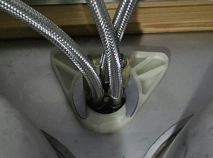 Flexibla metallslangar som är installerade vid en röranslutning, på en yta av trä och metall.