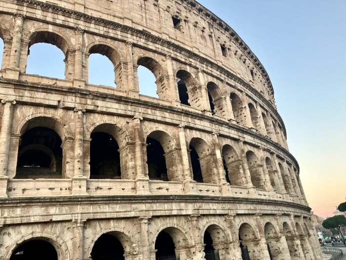 Det romerska Colosseum i solnedgången med tydliga rundbågar på flera våningar, delvis upplyst mot en klar himmel.