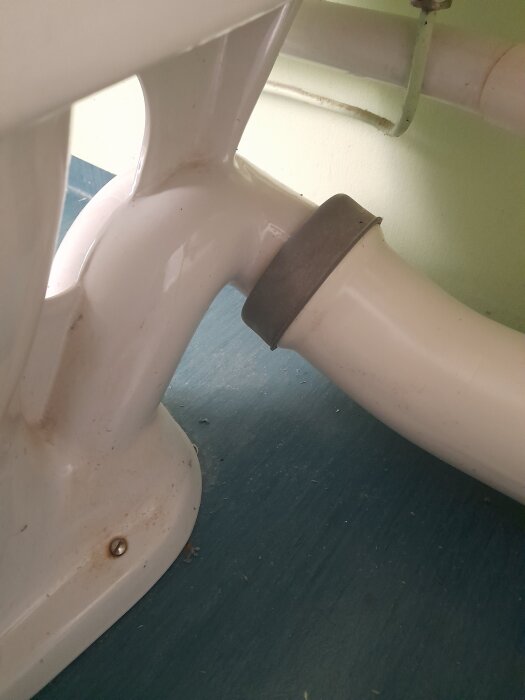 Toalettens avlopp anslutet med ett vitt rör och gummipackning syns mot ett blått golv.
