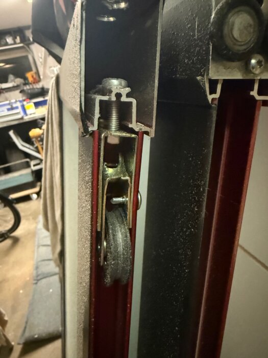 Närbild av mekanismen på en skjutdörr med synlig röd foliering och metallhjul i en garageverkstadsmiljö.
