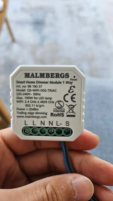 Smart dimmermodul från Malmbergs visas i handen, med modellinfo och anslutningsterminaler för elinstallation.
