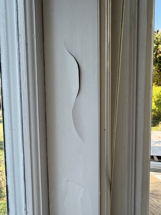 Flagnande vit färg på en fönsterkarm som lossnar i sjok, med ett synligt sprickmönster på en gammal träyta.